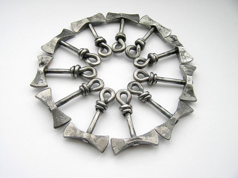 May include: A set of twelve silver metal axe-shaped bottle openers arranged in a circle. The axe heads are connected by a loop at the top.