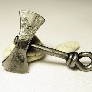 May include: A silver-colored metal axe pendant with a knotted handle. The axe head has a double-bladed design.