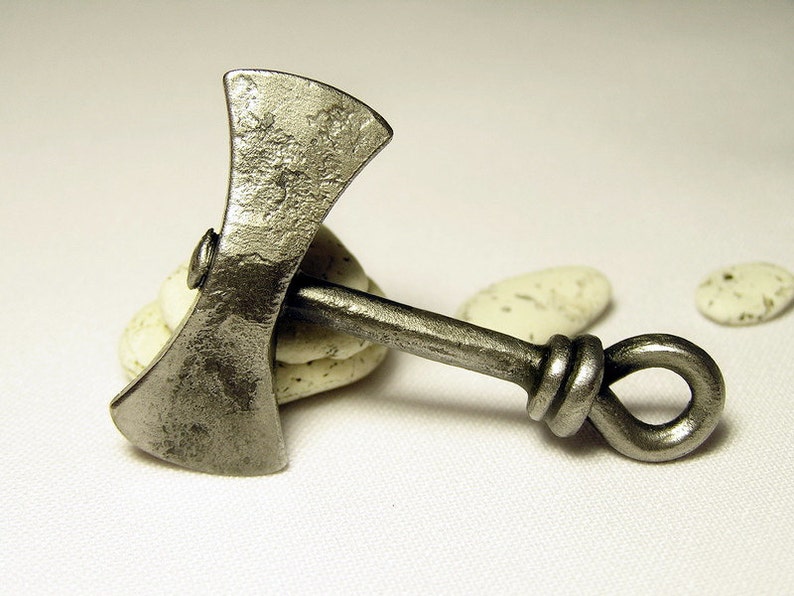May include: A silver-colored metal axe pendant with a knotted handle. The axe head has a double-bladed design.