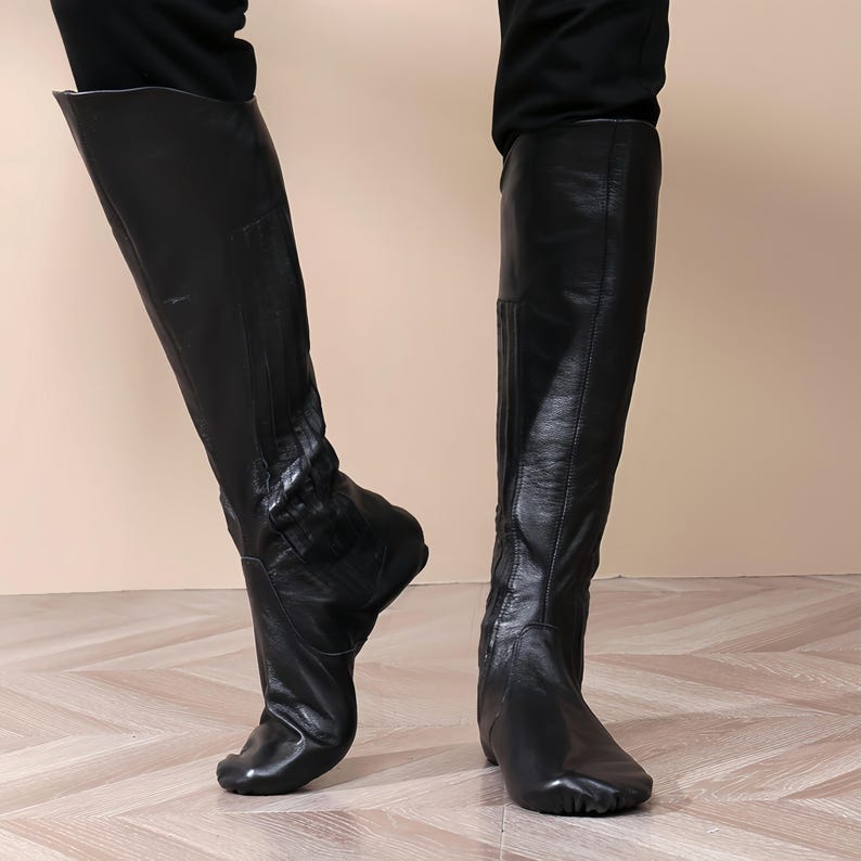 A pair of black leather boots with a high heel, worn by a person standing on a wooden floor.