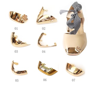 May include: A collection of gold-colored metal shoe and bag hardware. The hardware includes decorative corner pieces, a toe cap with a rose, and a piece with the word "Fancy". The image also shows a beige shoe with a gold toe cap and a black and white striped bow.