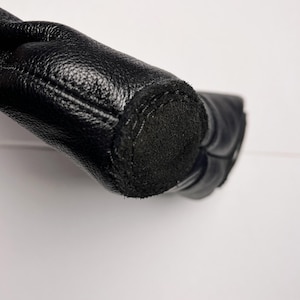 A close-up view of a black leather boot or shoe, with a black sole visible.