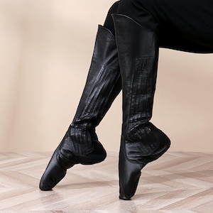 A pair of black leather ballet shoes with pointed toes and a high heel, worn by a person.