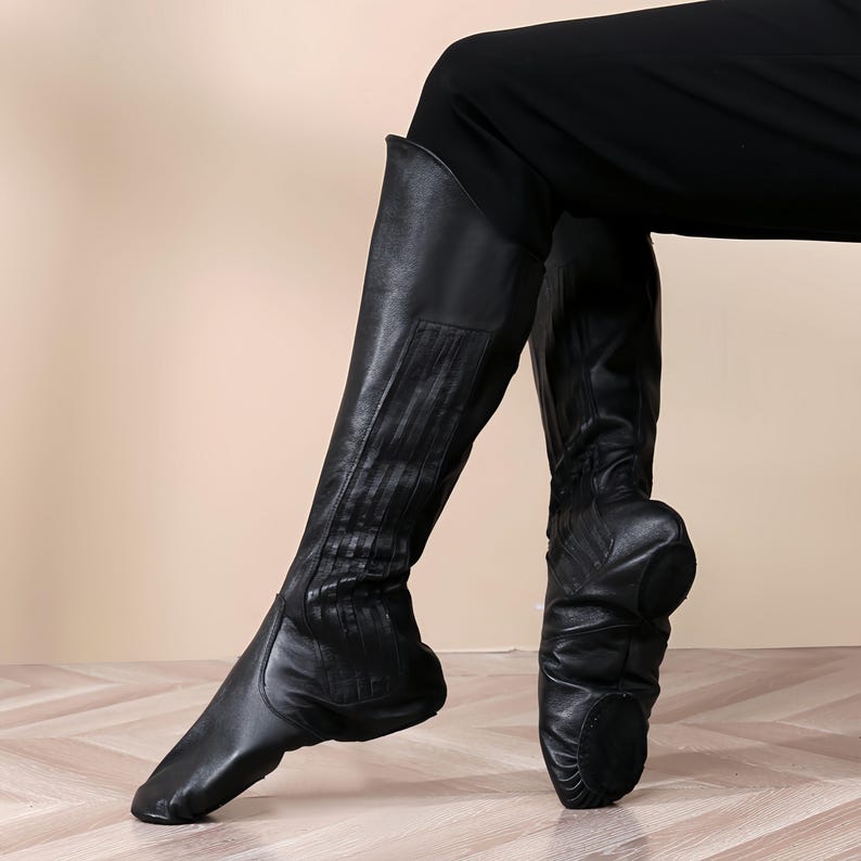 A close-up of a person's legs wearing black leather boots, with the boots positioned on a wooden floor.
