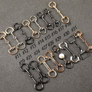 May include: A collection of 18 gold and black metal  horse bit style clasps, with numbers 11 through 31 printed below each clasp.