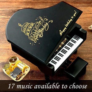 May include: A black miniature piano music box with a gold-colored "Happy Birthday" cake design. The piano keys are white and black. The text "Happy birthday to you!" is written on the top. The text "17 music available to choose" is at the bottom.
