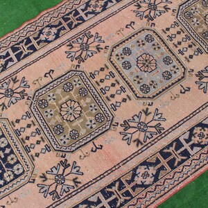 May include: A vintage pink and blue rug with a geometric pattern. The rug has a border of black and white geometric shapes.