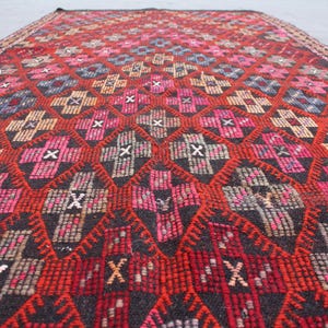 May include: A red, black, and white patterned rug with a geometric design. The rug is woven with a variety of textures and colors.