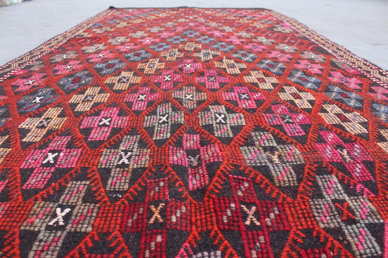 May include: A red, black, and white patterned rug with a geometric design. The rug is woven with a variety of textures and colors.
