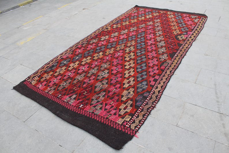 May include: A traditional Turkish rug with a geometric pattern in shades of red, brown, and black. The rug has a dark brown background with intricate details woven into the design.