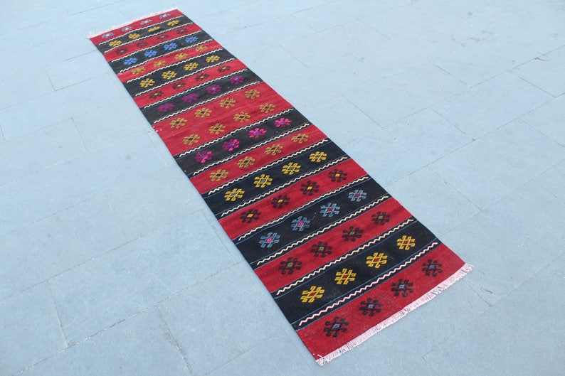 May include: A long, narrow red and black rug with a geometric pattern. The rug has a fringe on both ends.