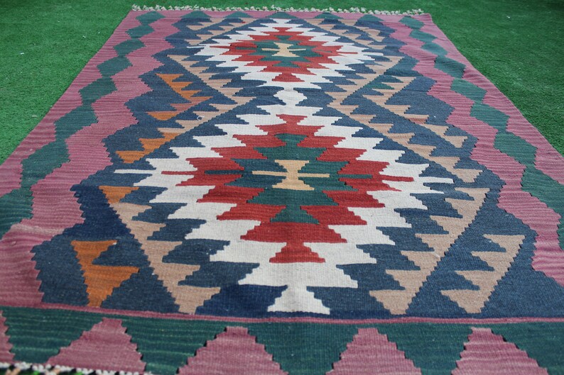 Puede incluir: Una alfombra tradicional con un patr&oacute;n geom&eacute;trico en tonos rojos, azules, verdes y marrones. La alfombra tiene un borde con flecos y est&aacute; tejida con una variedad de texturas.
