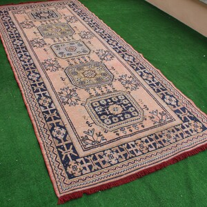 May include: A vintage pink and blue rug with a geometric pattern. The rug has a fringe border and is made of wool.