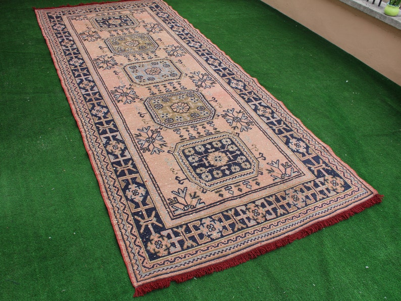 May include: A vintage pink and blue rug with a geometric pattern. The rug has a fringe border and is made of wool.