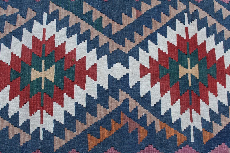 Puede incluir: Primer plano de una alfombra tejida colorida con un patr&oacute;n geom&eacute;trico en tonos de rojo, blanco, azul, verde y marr&oacute;n.