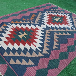 Puede incluir: Una alfombra colorida con un patr&oacute;n geom&eacute;trico en tonos de rojo, verde, azul y blanco. La alfombra tiene un borde de flecos y est&aacute; hecha de lana.