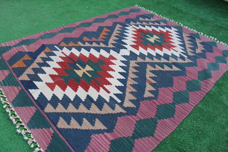 Puede incluir: Una alfombra colorida con un patr&oacute;n geom&eacute;trico en tonos de rojo, verde, azul y blanco. La alfombra tiene un borde de flecos y est&aacute; hecha de lana.