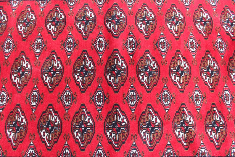 Puede incluir: Alfombra roja con un patr&oacute;n repetitivo de formas geom&eacute;tricas marrones, blancas y negras.