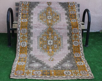 May include: A vintage pink and yellow rug with a geometric pattern. The rug has a fringe border and is laid out on a bench.