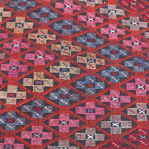 May include: A close-up of a colorful rug with a geometric pattern. The rug is made of wool and has a black background with red, blue, and pink accents.