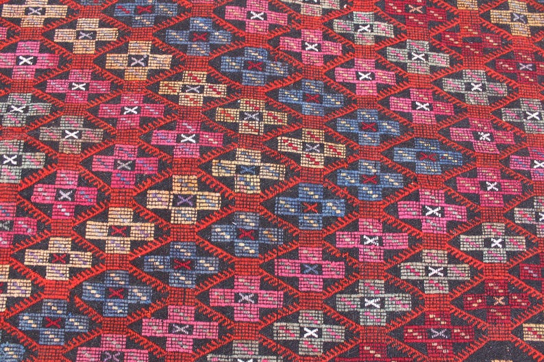 May include: A close-up of a colorful rug with a geometric pattern. The rug is made of wool and has a black background with red, blue, and pink accents.