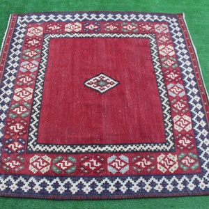 May include: A red, blue, and white patterned rug with a geometric design. The rug has a central diamond shape with a smaller diamond inside. The rug is surrounded by a border of smaller geometric shapes.