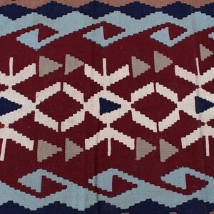 May include: A close-up of a red, white, blue, and gray patterned rug with a geometric design. The rug has a woven texture.
