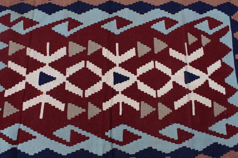 May include: A close-up of a red, white, blue, and gray patterned rug with a geometric design. The rug has a woven texture.