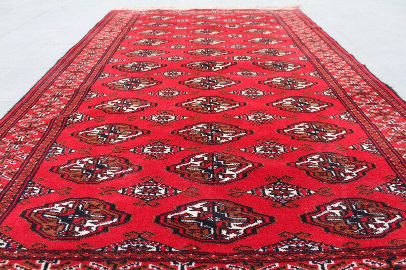 Puede incluir: Una alfombra roja con un dise&ntilde;o persa tradicional. La alfombra tiene un borde negro y patrones intrincados en tonos de marr&oacute;n y blanco.