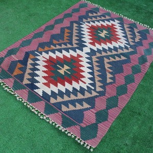 Puede incluir: Una alfombra colorida con un patr&oacute;n geom&eacute;trico en tonos de rojo, verde, azul y blanco. La alfombra tiene un borde de flecos y est&aacute; colocada sobre una superficie verde.