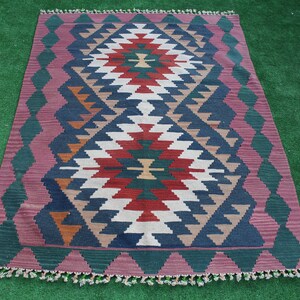Puede incluir: Una alfombra colorida con un patr&oacute;n geom&eacute;trico en tonos de rojo, verde, azul, blanco y marr&oacute;n. La alfombra tiene un borde de flecos y est&aacute; colocada sobre una superficie verde.