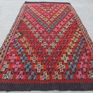 May include: A traditional Turkish rug with a geometric pattern in shades of red, pink, blue, and beige. The rug has a black background and a fringe border.