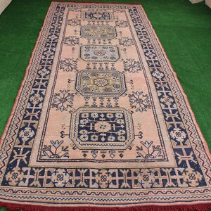 May include: A vintage rug with a pink background and intricate blue, black, and gold patterns. The rug has a fringe border.