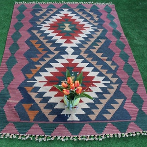 Puede incluir: Una alfombra colorida con un patr&oacute;n geom&eacute;trico en tonos de rojo, azul, verde y blanco. La alfombra tiene un borde de flecos y est&aacute; colocada sobre una superficie verde.