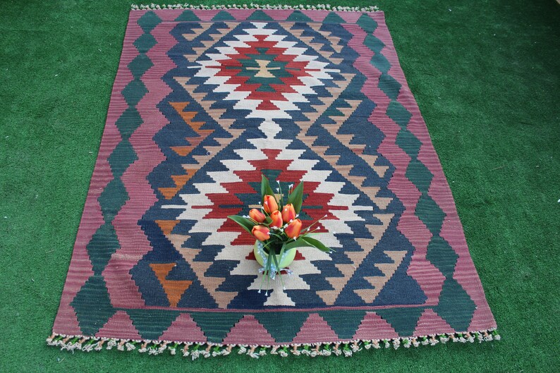 Puede incluir: Una alfombra colorida con un patr&oacute;n geom&eacute;trico en tonos de rojo, azul, verde y blanco. La alfombra tiene un borde de flecos y est&aacute; colocada sobre una superficie verde.