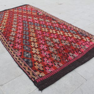 May include: A red, pink, and black patterned rug with a geometric design. The rug has a dark brown border.