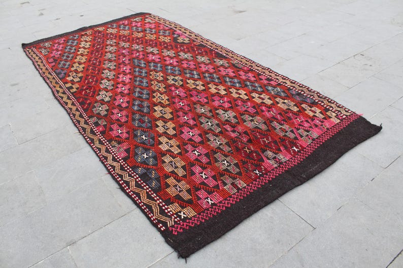May include: A red, pink, and black patterned rug with a geometric design. The rug has a dark brown border.