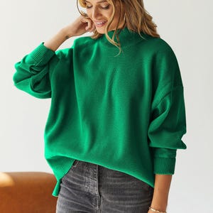 Puede incluir: Un su&eacute;ter de cuello alto verde brillante con mangas largas y un ajuste holgado.