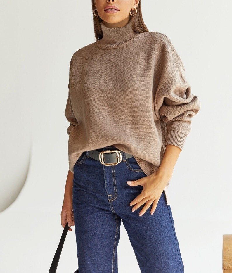 Puede incluir: Un su&eacute;ter de cuello alto marr&oacute;n con mangas largas y un corte holgado. El su&eacute;ter se combina con jeans azul oscuro y un cintur&oacute;n negro con hebilla dorada.