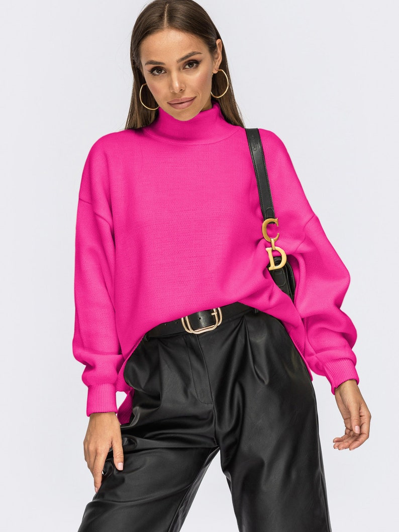 Puede incluir: Un su&eacute;ter de cuello alto de color rosa brillante con mangas largas y un corte holgado. El su&eacute;ter se combina con pantalones de cuero negro y un cintur&oacute;n dorado.