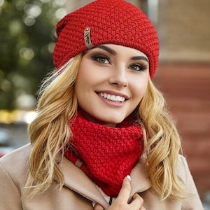 Peut inclure: Un bonnet et un tour de cou assortis en tricot rouge. Le bonnet a une petite étiquette marron avec le mot "Optima" dessus.