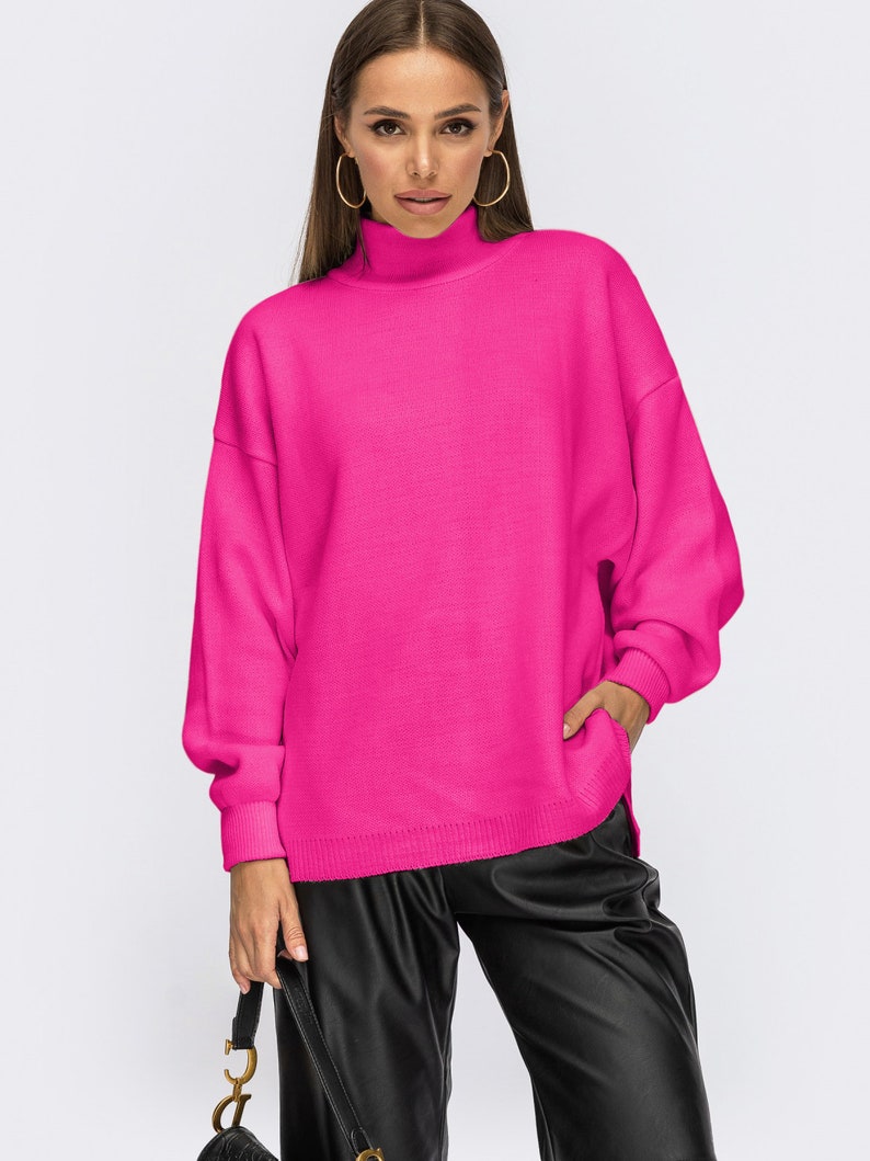 Puede incluir: Un jersey de cuello alto de color rosa brillante con mangas largas y un corte holgado.