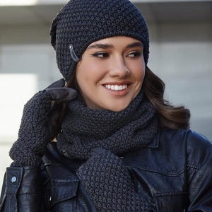 Könnte beinhalten: Ein Set aus grauer Strickmütze, Schal und Handschuhen. Die Mütze hat einen umgeschlagenen Bund und einen kleinen silbernen Akzent. Der Schal ist lang und schmal. Die Handschuhe sind fingerlos.