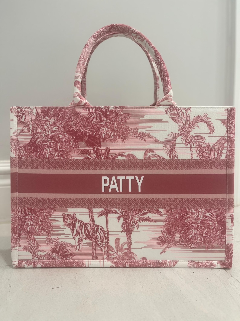 May include: A red and white tote bag with a jungle scene print, featuring a tiger and palm trees. The bag has a red band with the name "PATTY" in white letters. It has a rectangular shape with two handles.