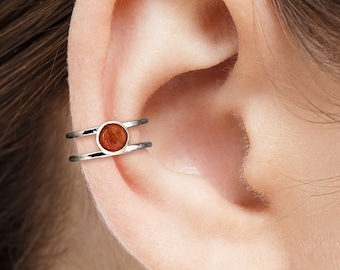 May include: A silver ear cuff with a double band and a round brown stone in the center.