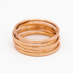 May include: A set of five thin gold-toned stacking rings. The rings are hammered and have a slightly irregular texture.
