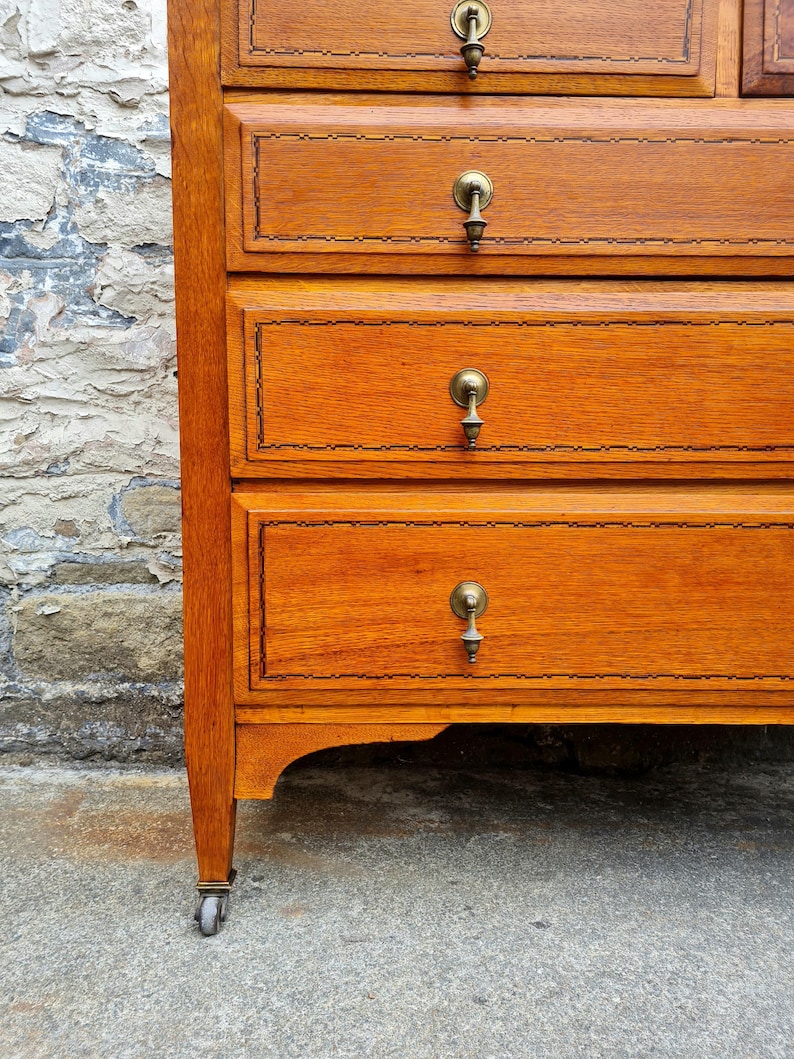 May include: A close-up of a wooden dresser with four drawers. The dresser is made of light brown wood with brass handles and decorative trim. The bottom of the dresser has a curved design, and the legs have small wheels.
