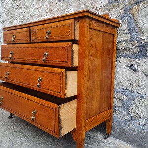 May include: A vintage wooden dresser with multiple drawers, some open. The dresser is a warm brown color with brass hardware and sits on small caster wheels. The drawers have decorative trim.