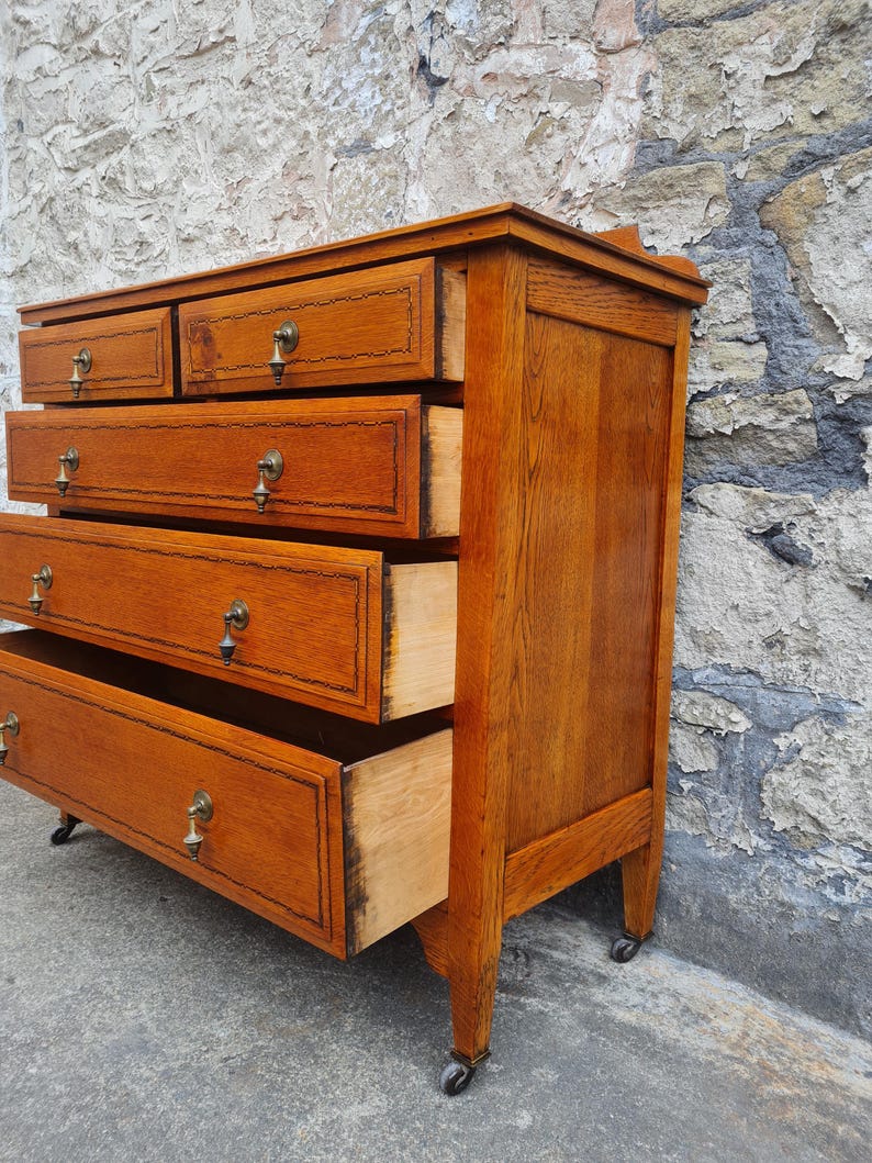 May include: A vintage wooden dresser with multiple drawers, some open. The dresser is a warm brown color with brass hardware and sits on small caster wheels. The drawers have decorative trim.