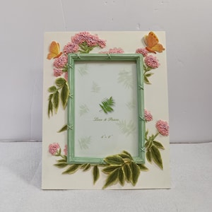 May include: A rectangular photo frame with a light green inner frame and a cream-coloured outer frame. It's decorated with pink flowers, green leaves, and two orange butterflies. The text "Love & Peace" and "4 x 6" are visible.
